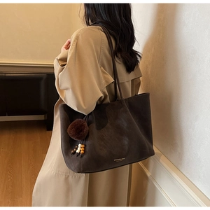 Detail of dark brown faux leather tote bag with plush charm and gold logo lettering
