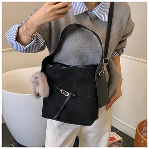 Detail of black textured bucket bag with silver buckle and plush bunny charm accessory