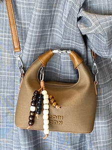 Brown leather handbag with arc handle and bead charm worn over blue plaid coat