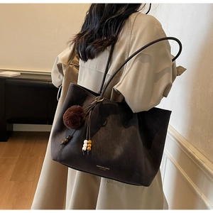 Detail of soft dark brown suede tote bag featuring a decorative fur pompom and wooden beads