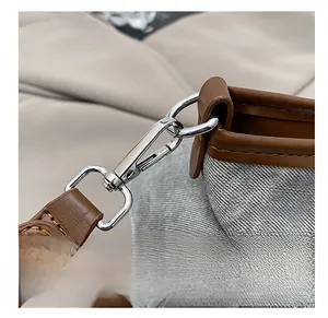 Gros plan sur le crochet en métal argenté et la bandoulière en cuir brun du sac gris