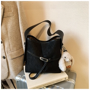 Detail of black textured bucket bag with white bunny plush charm and adjustable strap