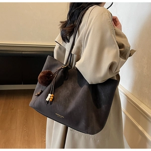 Close-up of deep brown suede tote bag featuring a decorative plush ball and wood bead charm