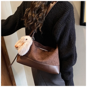 Detail of a brown shoulder bag with pleated texture and a cute white plush bunny charm