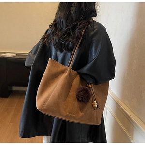Detail view of large brown suede tote bag with plush ball charm and beaded strap decor