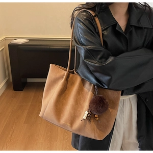 Detail of caramel suede tote bag with plush ball charm and gold fashion logo