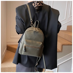 Detail view of a dark olive green minimalist backpack with golden zipper hardware on model