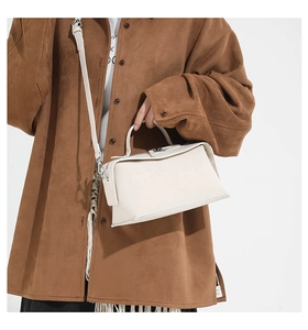 Close-up of a cream-white geometric leather handbag held against a brown suede shirt