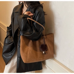 Detail of a brown suede tote bag with leather straps and a decorative plush charm