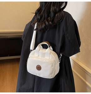 Detail of white nylon square crossbody bag with brown leather logo patch and zip pockets