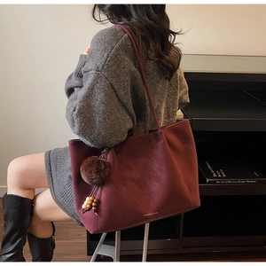 Detail of burgundy tote bag with brown pompom charm and elegant wooden beads