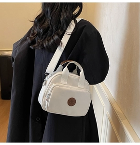 Detail view of a white canvas crossbody bag with round leather logo and wide fabric strap