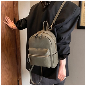 Detail of olive green vintage backpack featuring white stitching and gold metal zippers