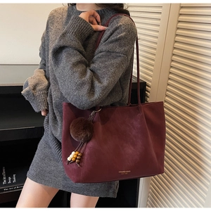 Detail of burgundy suede tote bag featuring golden logo and plush pompom charm