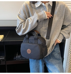 Detail of black nylon crossbody bag with brown leather handles and multi-zipper pockets