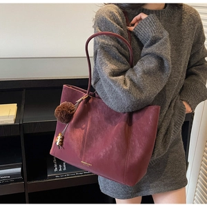 Detail of burgundy matte tote bag with plush charm and golden logo on soft faux leather