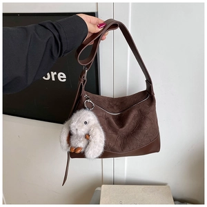 Close-up of dark brown pleated hobo bag with silver zipper and plush rabbit charm