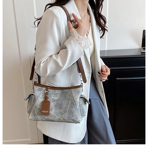 Détail d'un sac à bandoulière gris avec finitions en cuir marron sur un blazer blanc