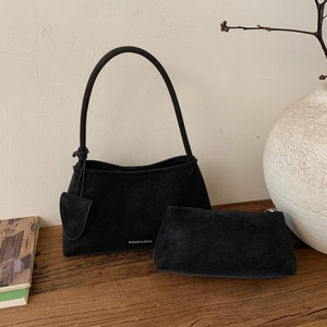 Close-up of black suede underarm bag and matching pouch on a rustic wooden surface