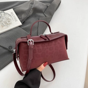 Detail view of burgundy leather pillow bag with subtle leopard texture and dual zippers