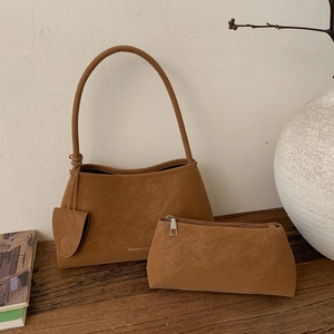 Close-up of brown suede handbag set with fashion text on a minimalist wooden table