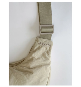 Detailed close-up of beige nylon dumpling bag showing WISDORA embroidery and adjustable strap