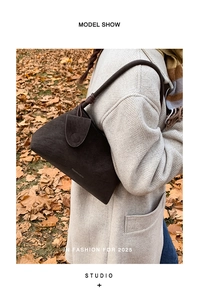 Detailed close-up of dark brown suede shoulder bag with unique buckle and knot strap detail