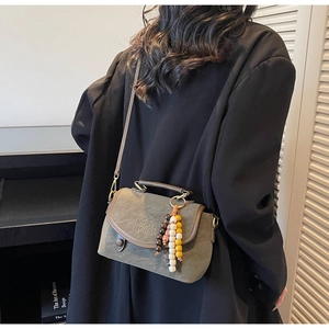 Detail of grey-green vintage leather crossbody bag with beaded charm and brand embossing