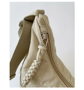 Detail of smooth zipper closure with woven cord puller on beige nylon crossbody tote bag