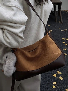 Brown pleated leather crossbody bag with rabbit charm shown in an autumn street setting