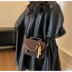 Detail of dark brown matte leather bag with vintage wooden bead charm and embossed logo