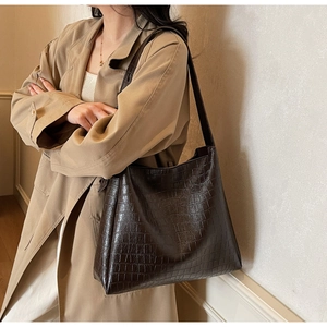 Detail of dark brown faux crocodile leather tote bag worn with a casual khaki trench coat