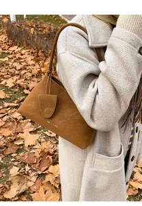 Detail of caramel suede shoulder bag with fashion lettering and shield charm on coat