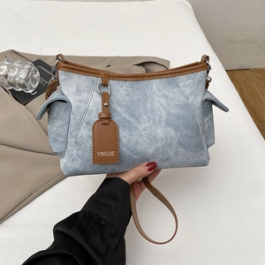 Détail de la texture denim bleu clair et des finitions en cuir marron sur le sac porté épaule