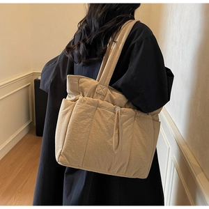Detail view of a quilted beige tote bag showing side pocket and drawstring toggle on nylon fabric