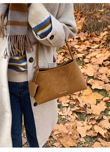 Close-up of brown suede shoulder bag with coin pouch against autumn maple leaves