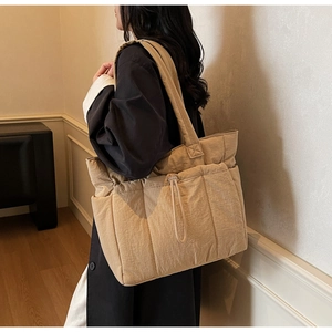 Quilted nylon tote bag in beige shown on shoulder, featuring drawstring pocket detail