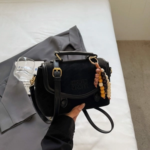Close-up of black matte leather handbag featuring gold hardware and colorful wood bead charm