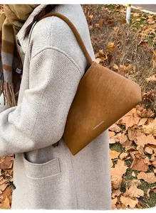 Close-up of brown suede shoulder bag with Fashion & Bags lettering on autumn grass