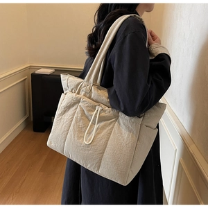 Detail view of a large cream quilted tote bag with drawstring on a female model