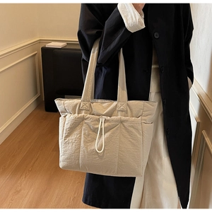 Detail of beige wrinkled nylon tote bag with drawstring pocket on black wool coat