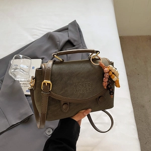 Close-up of olive green vintage handbag with gold buckles and beaded charm on white bedding