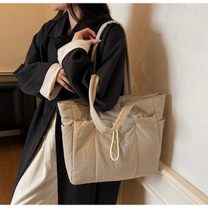 Detail view of a large beige tote bag featuring side pockets and drawstring details