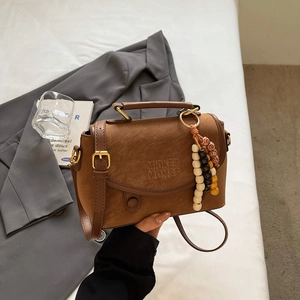 Detail of a brown matte crossbody bag with wooden bead tassels and logo embossing