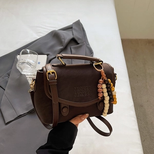 Detail of dark brown vintage leather handbag with litchi texture and beaded charm