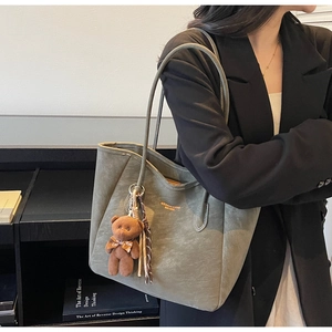 Close-up of sage green tote bag featuring golden logo and cute teddy bear pendant