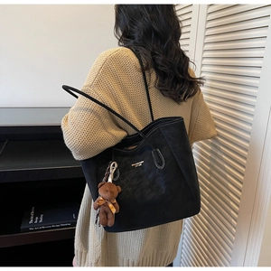 Detail of black suede tote bag featuring contrast stitching and a cute bear bag charm