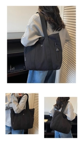 Detail of the black canvas tote bag showing its wide shoulder strap and side zipper pocket