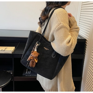 Close-up of black suede tote bag with golden logo and cute brown teddy bear keychain