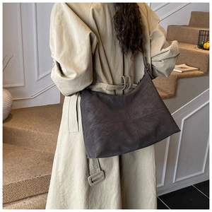 Detail of dark brown suede hobo bag with cross stitching worn with a beige trench coat